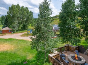 Eine Terrasse mit Feuerstelle, Sitzgelegenheiten im Freien und Blick auf einen Wald.