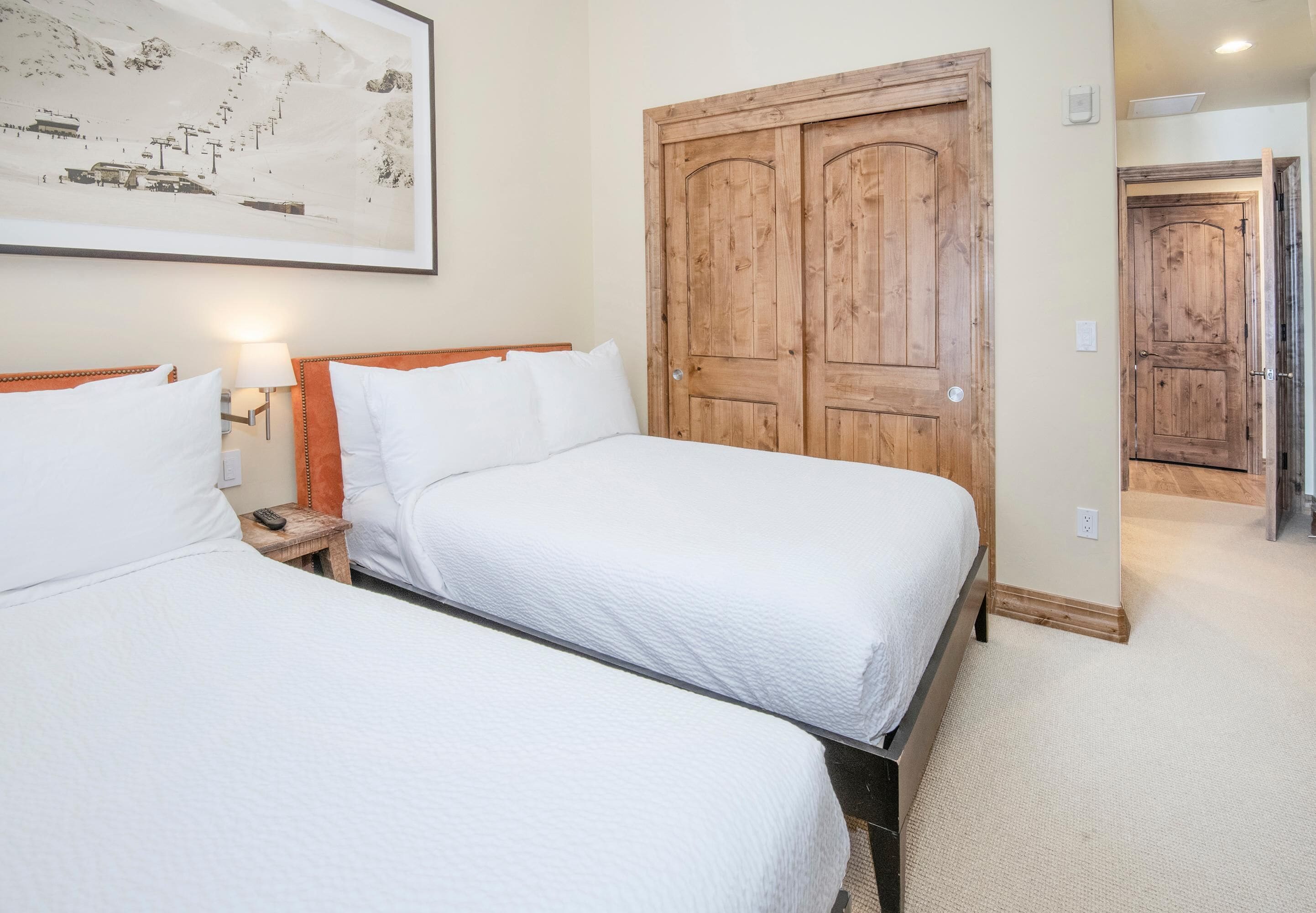 A hotel room with two beds, a wooden wardrobe, a framed picture on the wall, and a carpeted floor.