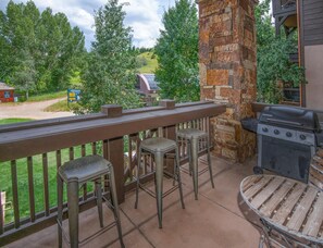 An outdoor patio with a stone wall, a grill, and two stools. - Beaver Creek Landing A204, 3BD 3.5ba Ski In/out Condo (Avon)