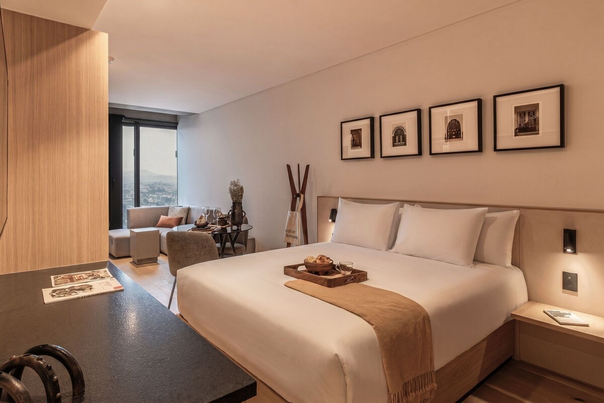 Una camera d'albergo con un letto grande, un tavolo da pranzo, un divano e vista sulla città.