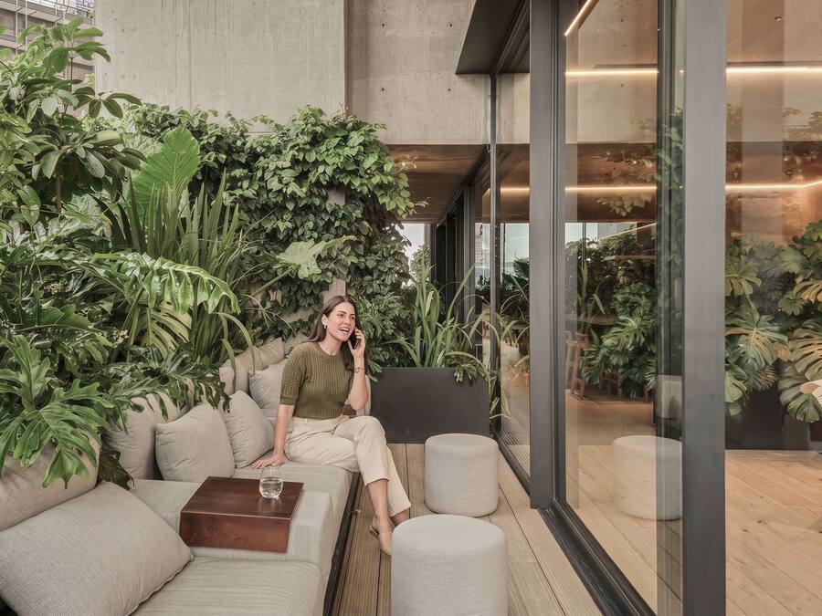 Un espacio interior moderno con un sofá, un reposapiés y un separador de vidrio.