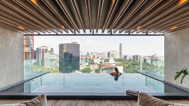 Une piscine à débordement moderne située sur le toit, offrant une vue sur la ville, avec un revêtement de sol en bois et deux canapés.