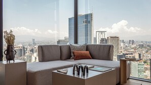 Un salon moderne avec un canapé d’angle, une table basse et une vue sur le paysage urbain grâce à de grandes fenêtres.