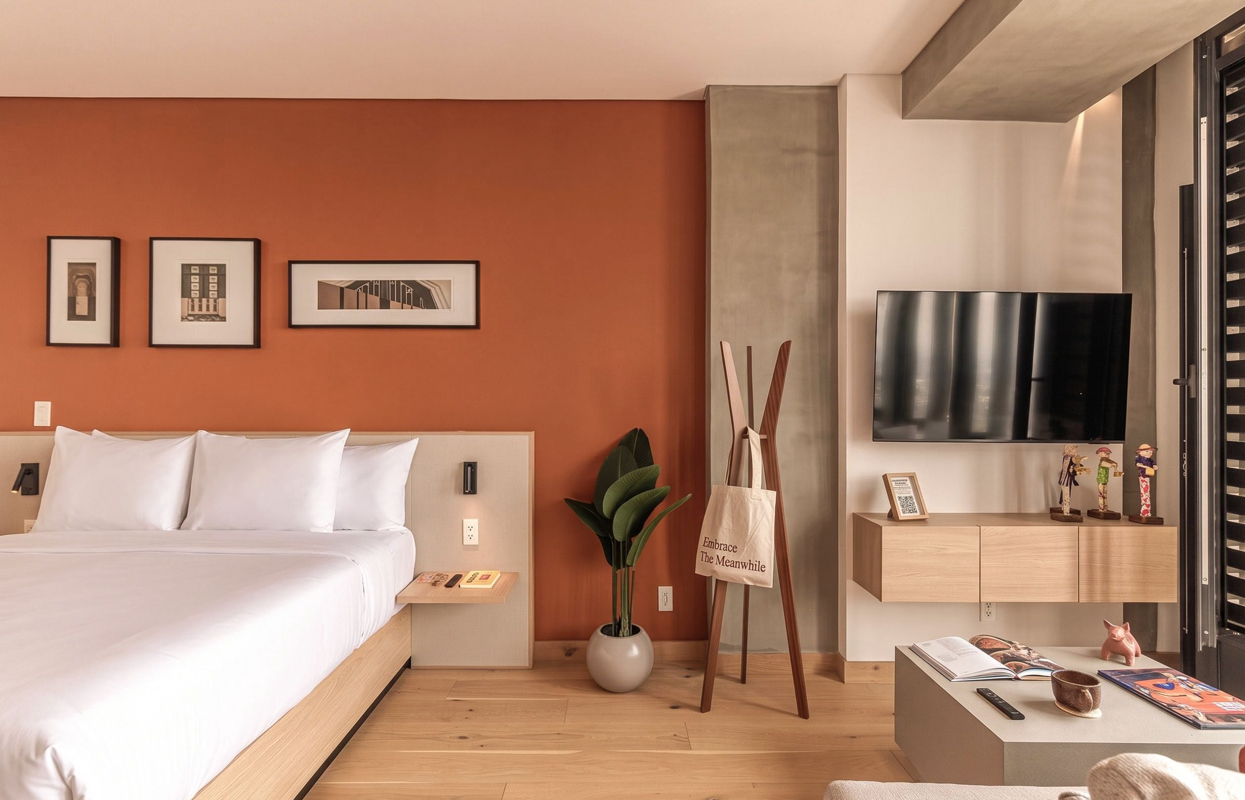A modern hotel room with a large bed, a flat-screen TV, a wooden nightstand, and a potted plant.