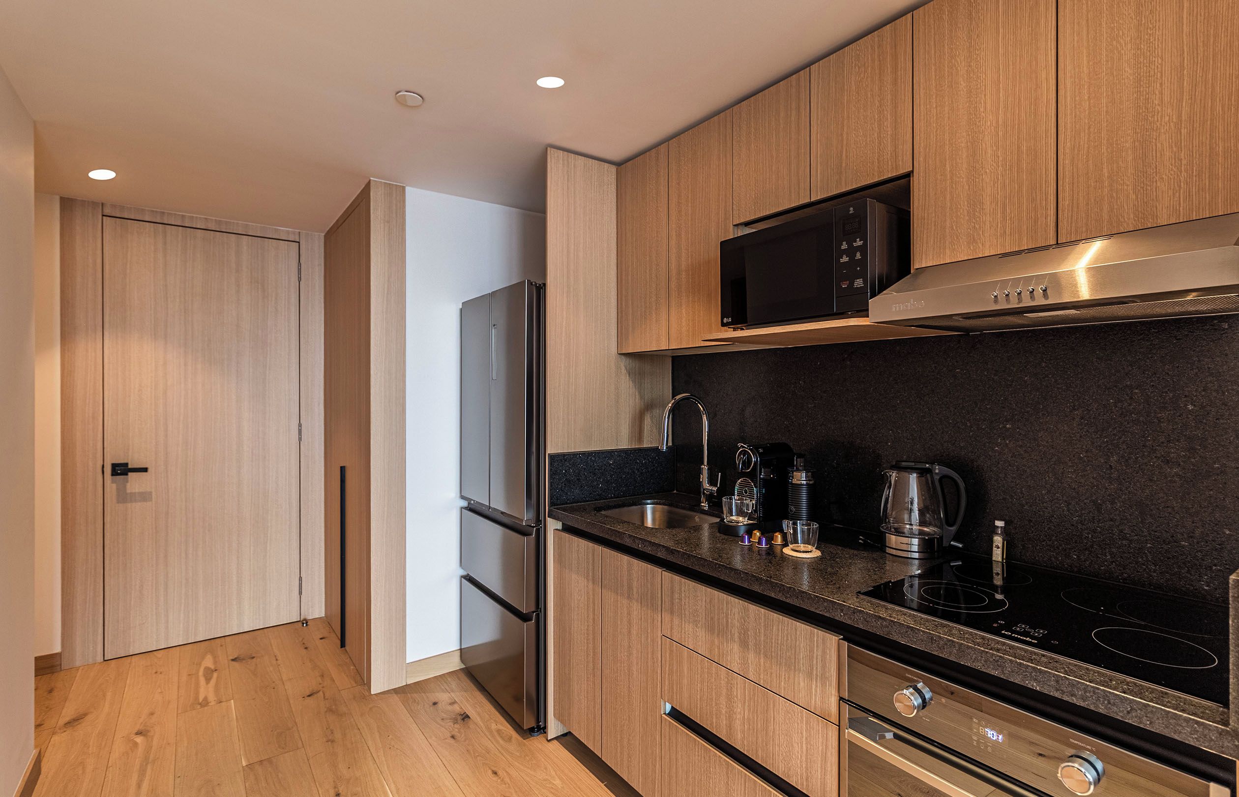 Eine moderne Küche mit Holzschränken, einem Edelstahlkühlschrank, einer Mikrowelle, einer Kaffeemaschine und einem Gaskochfeld.