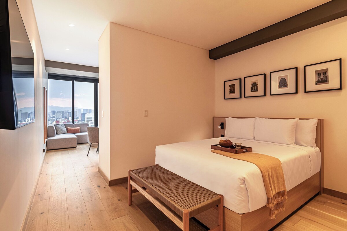 Una camera da letto moderna con un grande letto, una panca e vista sulla città.