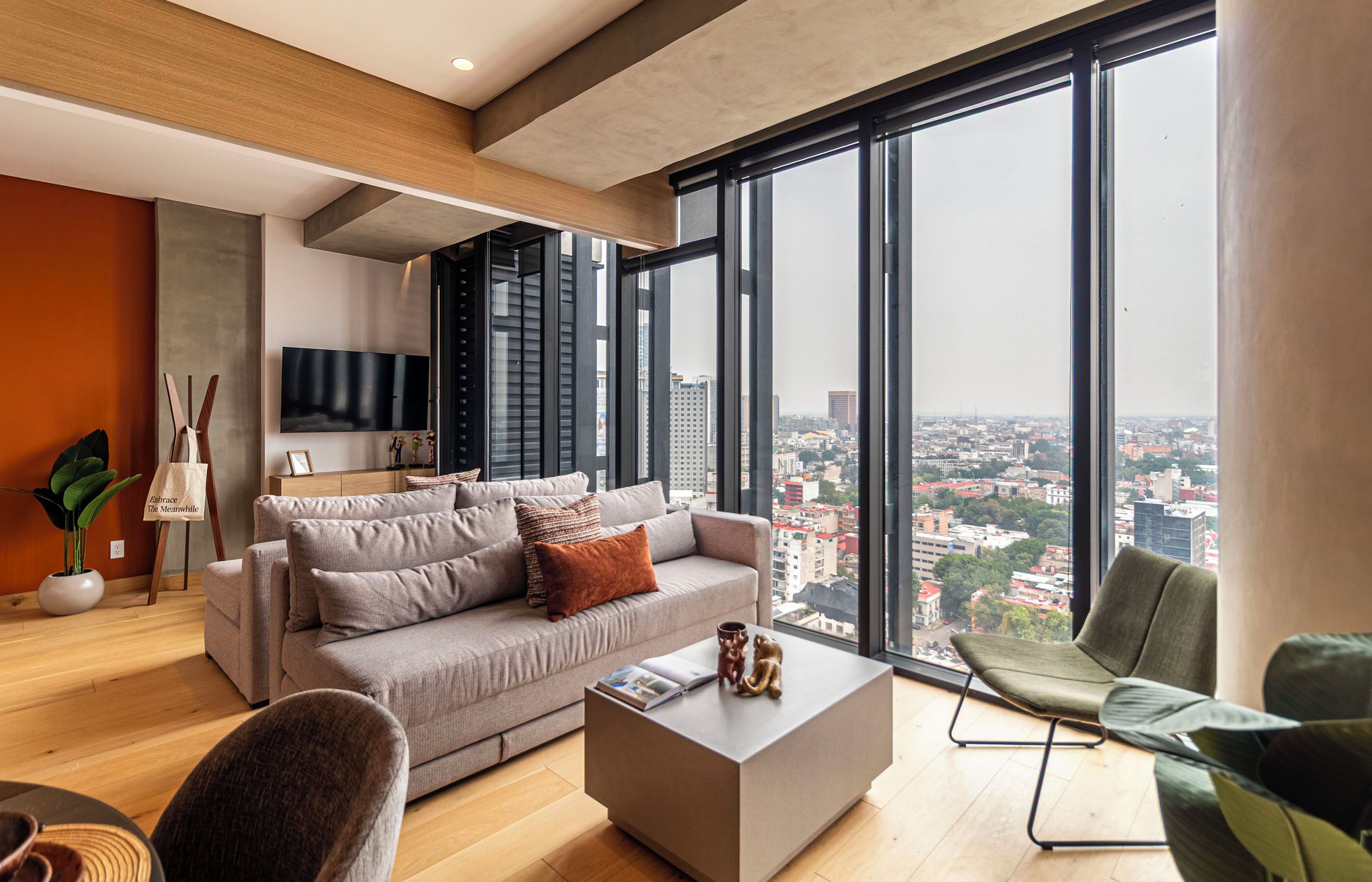 Un salon moderne avec une grande fenêtre, un canapé gris, une table basse et une vue sur le paysage urbain.