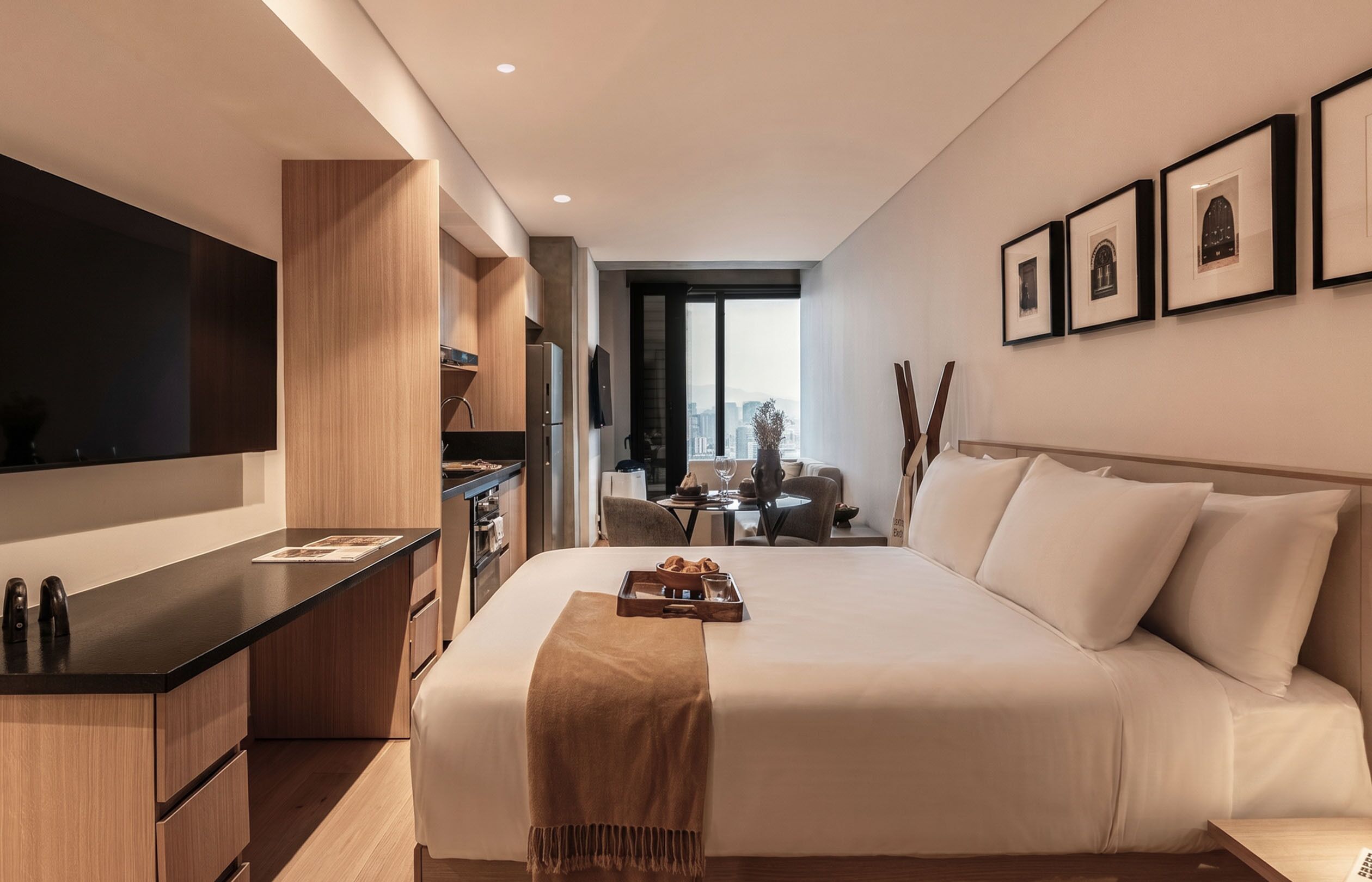 Une chambre d’hôtel moderne dotée d’un grand lit, d’une télévision à écran plat, d’une kitchenette et offrant une vue sur la ville.