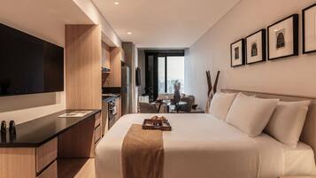 Une chambre d’hôtel moderne dotée d’un grand lit, d’une télévision à écran plat, d’une kitchenette et offrant une vue sur la ville.