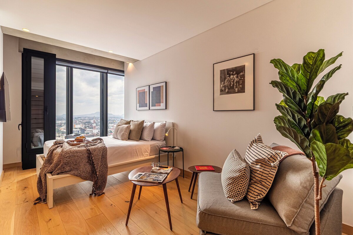 Una sala de estar moderna con una cama, un sofá, una mesa de centro y una planta grande.
