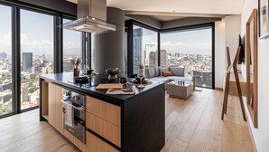 Une cuisine moderne dotée d’un grand îlot central, d’un four encastré et offrant une vue sur le paysage urbain grâce à de grandes fenêtres.
