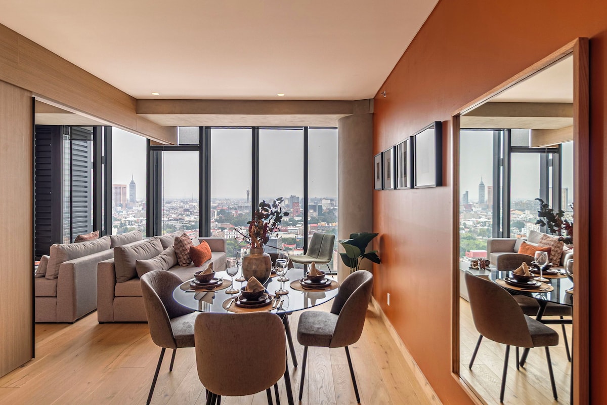 Un comedor moderno con vistas a la ciudad, un sofá y una mesa de comedor dispuesta para cuatro personas.