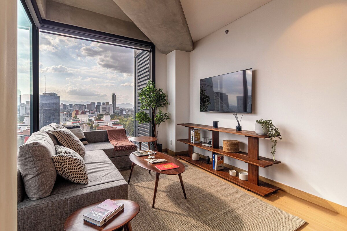 Una sala de estar moderna con un ventanal grande, un sofá, una mesa de centro y un televisor en la pared.