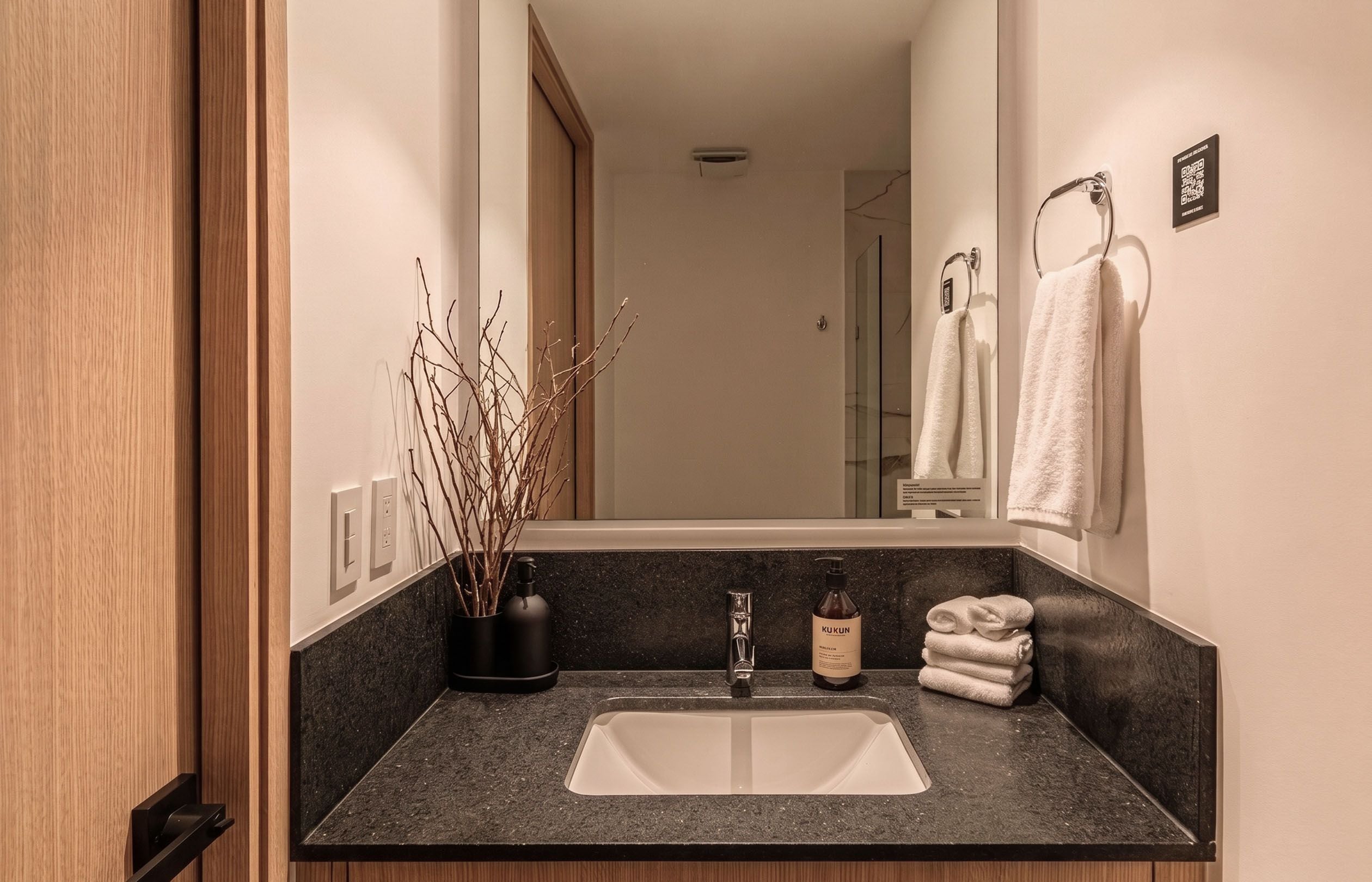 Un baño moderno con un lavamanos, un espejo, un perchero para toallas y una rama decorativa.