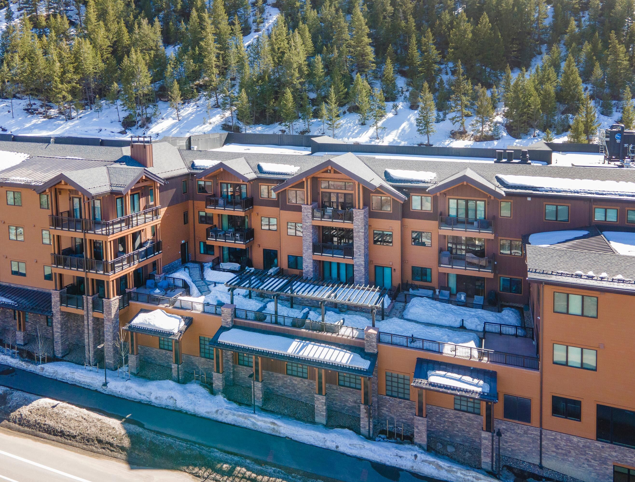 A multi-story hotel with balconies, a ski slope in the background, and a river in the foreground.