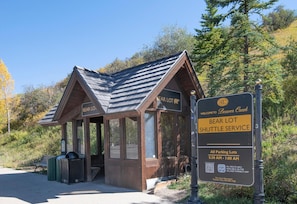 Eine Holzhütte mit der Aufschrift 'Bear Lot Shuttle Service', in der Nähe befinden sich eine Bank und ein Mülleimer.