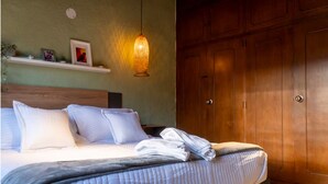 Een netjes opgemaakt bed met kussens en een gevouwen handdoek, een houten garderobe en een wandplank met decoratieve objecten.