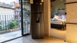 Een balkon met een metalen hekwerk, een roestvrijstalen koelkast en een bed met wit beddengoed.
