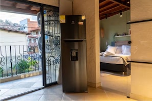A balcony with a metal gate, a stainless steel refrigerator, and a bed with white bedding. - Modern Suite with Private Balcony • A/C • WiFi (Medellín)