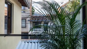 Un balcone con vista sugli edifici circostanti, una pianta in vaso e un tenda da sole retrattile con luci pendenti.