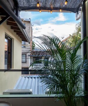 A balcony with a view of neighboring buildings, a potted plant, and a retractable awning with hanging lights. - Modern Private Suite Terrace + Self Check-in (Medellín)