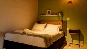 Un letto rifatto con cura, con una testiera in legno, un comodino e una mensola a parete con oggetti decorativi.