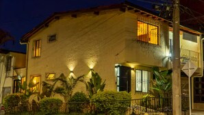 Un edificio a due piani con un balcone, un ingresso carrabile e una facciata ben illuminata.