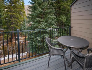 A balcony with a table and chairs, a metal railing, and a view of trees and a building in the background. - Timber Falls 304, 3BD East Vail Condo With Amenities (Vail)