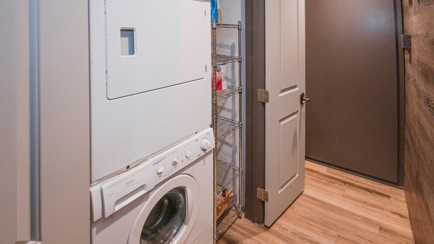 A laundry room with a front-loading washer and dryer, a metal shelf with a bottle, and a door leading to another room. - Creekside 3, 2BD + Loft in Heart of Vail Village (Vail)