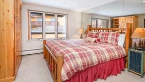 A bedroom with a wooden bed, a large window, a mirror, and a small bedside table. - Creekside 3, 2BD + Loft in Heart of Vail Village (Vail)