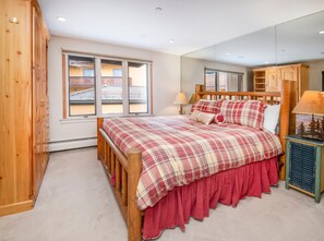 A bedroom with a wooden bed, a large window, a mirror, and a small bedside table. - Creekside 3, 2BD + Loft in Heart of Vail Village (Vail)