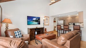 A living room with leather sofas, a coffee table, a TV, and a kitchen in the background. - Creekside 3, 2BD + Loft in Heart of Vail Village (Vail)