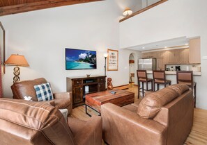 A living room with leather sofas, a coffee table, a TV, and a kitchen in the background. - Creekside 3, 2BD + Loft in Heart of Vail Village (Vail)