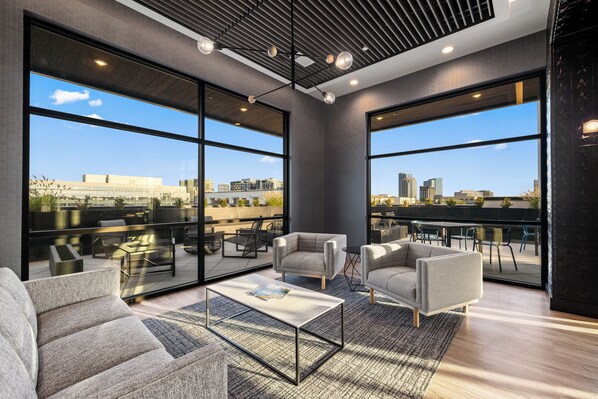 A modern interior with large windows, a sofa, a coffee table, and a city view. - Free Gated Parking • Music Row Condo • Pool • Rooftop Club Room with Pool Table (Nashville)