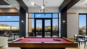A pool table in a room with large windows, modern furniture, and a city view. - Free Gated Parking • Music Row Condo • Pool • Rooftop Club Room with Pool Table (Nashville)