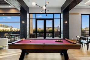 A pool table in a room with large windows, modern furniture, and a city view. - Free Gated Parking • Music Row Condo • Pool • Rooftop Club Room with Pool Table (Nashville)
