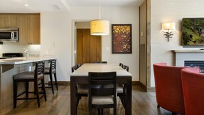 A modern kitchen with a dining area, wooden cabinets, a large island with a sink, and a fireplace. - Riverfront Resort & Spa 421a, 1BD Condo With Mtn Views (Avon)