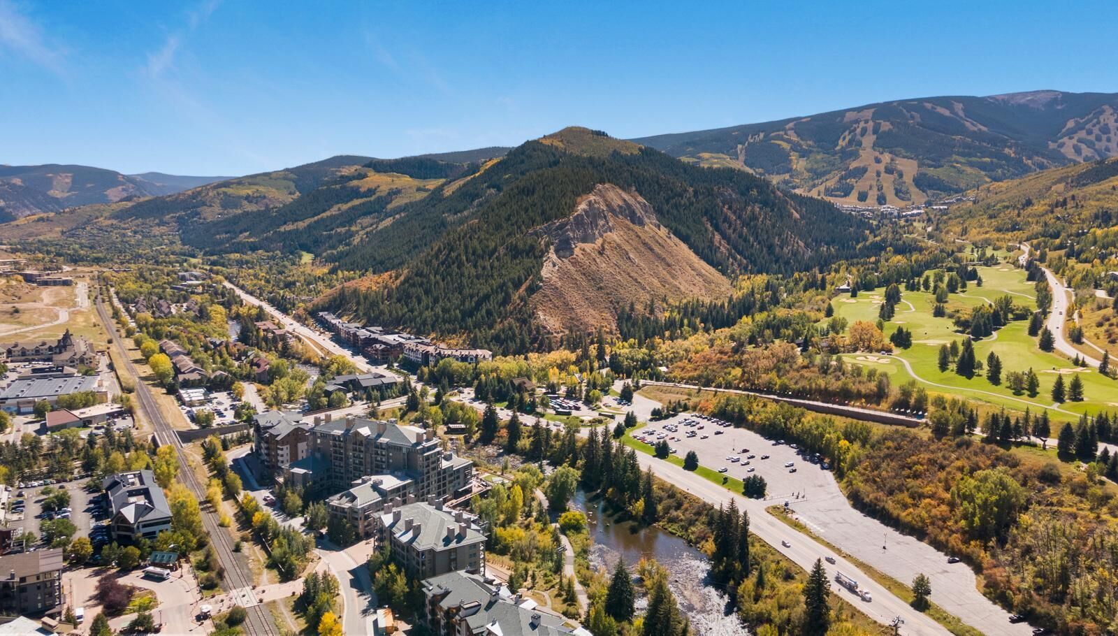 An aerial view of a town with a prominent mountain, a golf course, and a river.