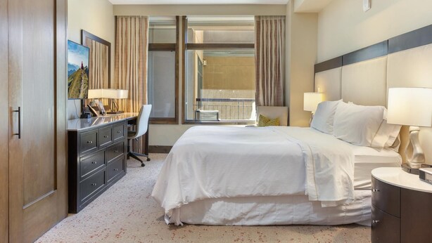A hotel room with a bed, desk, chair, and a large window with curtains. - Riverfront Resort & Spa 421a, 1BD Condo With Mtn Views (Avon)