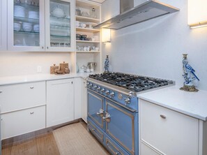 A kitchen with white cabinets, a blue stove, and glass-fronted shelves with dishes. - 725a Forest Road 4BD Home on Vail Mountain (Vail)