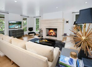 A modern living room with a fireplace, a sofa, a television, and a fireplace mantle. - 725a Forest Road 4BD Home on Vail Mountain (Vail)
