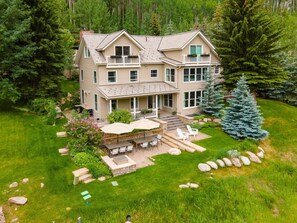 A two-story house with a patio, outdoor seating, and a large tree. - 725a Forest Road 4BD Home on Vail Mountain (Vail)