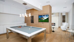 Moderni huone, jossa on biljardipöytä, seinälle asennettu televisio ja oleskelualue tuoleineen.