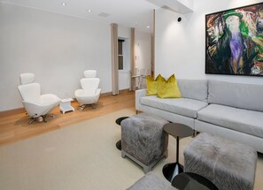 A modern living room with a grey sofa, two white chairs, a fluffy grey ottoman, and a painting on the wall. - 725a Forest Road 4BD Home on Vail Mountain (Vail)