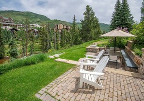 A patio with Adirondack chairs, a stone fire pit, and a view of a mountainous landscape. - 725a Forest Road 4BD Home on Vail Mountain (Vail)