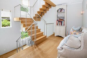 A staircase with wooden steps and metal railings, a white bookshelf filled with books, and a sofa with colorful pillows. - 725a Forest Road 4BD Home on Vail Mountain (Vail)