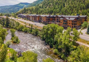 A multi-story lodge with balconies, a river, and forested hills in the background. - Frontgate 305, 3 BD Condo in Avon With Amenities (Avon)