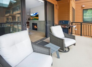 Ein Balkon mit Korbstühlen und einem Grill, ein Kamin mit Feuer und ein an der Wand montierter Fernseher.