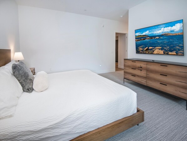 Ein Schlafzimmer mit Bett, Kommode, Nachttisch, Lampe und einem Gemälde einer Küstenlandschaft.