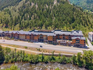 Ein mehrstöckiges Hotel mit einer Reihe von Balkonen, neben einer Straße und einem Fluss gelegen, umgeben von bewaldeten Hügeln.